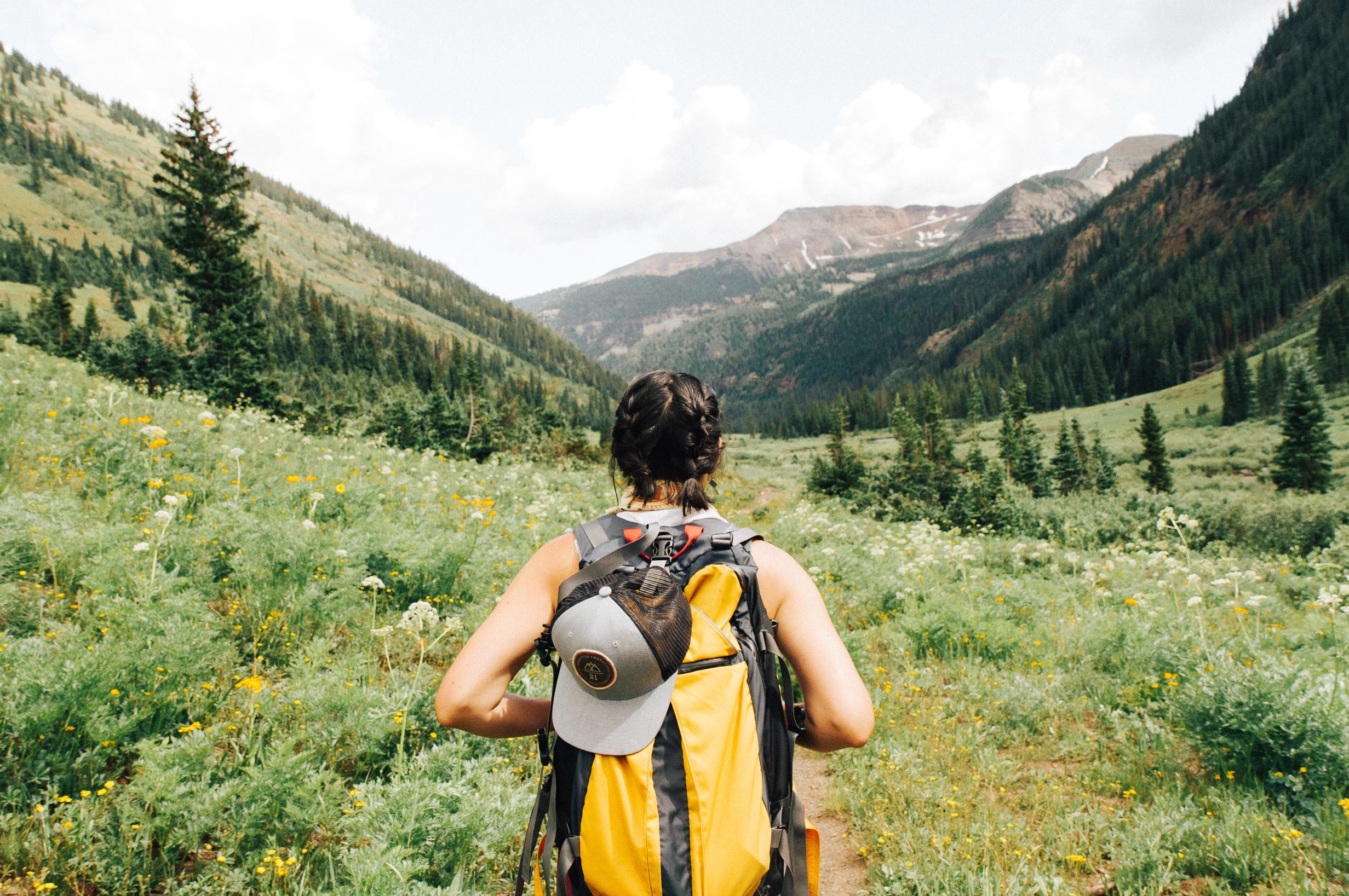 Stojąca na łące i zapatrzona w góry podróżująca po USA dziewczyna z plecakiem zwiedzająca jeden z amerykańskich parków narodowych, podziwia przyrodę.